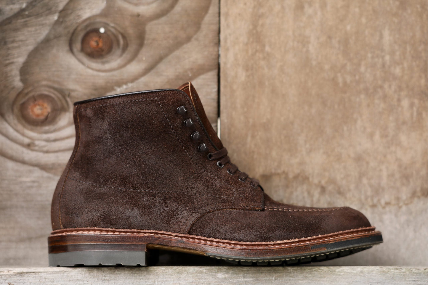 The Alden Madison 4015HC Indy Boot in Tobacco Reverse Chamois, featuring a commando sole and detailed stitching, is stylishly displayed against a wooden background, showcasing its rugged texture and sturdy appearance.