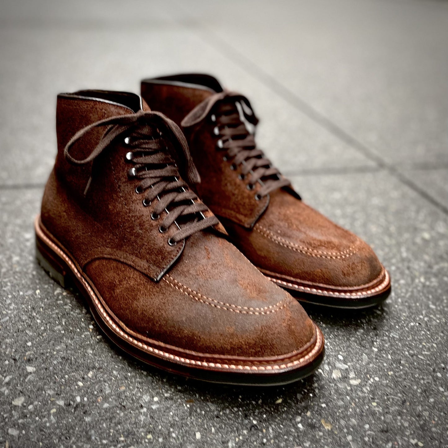 Alden Madisons 4015HC - Indy Boot in Tobacco Reverse Chamois features brown suede with dark laces, detailed toe stitching, and a sturdy commando sole. Set on a textured gray surface, these boots offer an elegant and rugged look.