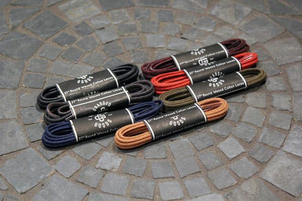 Nine pairs of Alden Madison Shoe Lace Guarded Goods, 27-inch waxed cotton laces in assorted colors, each wrapped with a black band, are displayed on a mosaic stone surface.