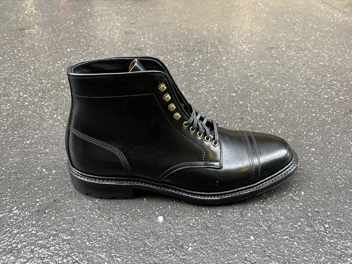 Positioned on a textured gray surface, the Alden Madison D9867HC-Stitchup 2/2 Boot in sleek Black Shell Cordovan features laces, metal eyelets, and a polished finish. The boots solid stitching showcases durability and style on its Commando Sole.