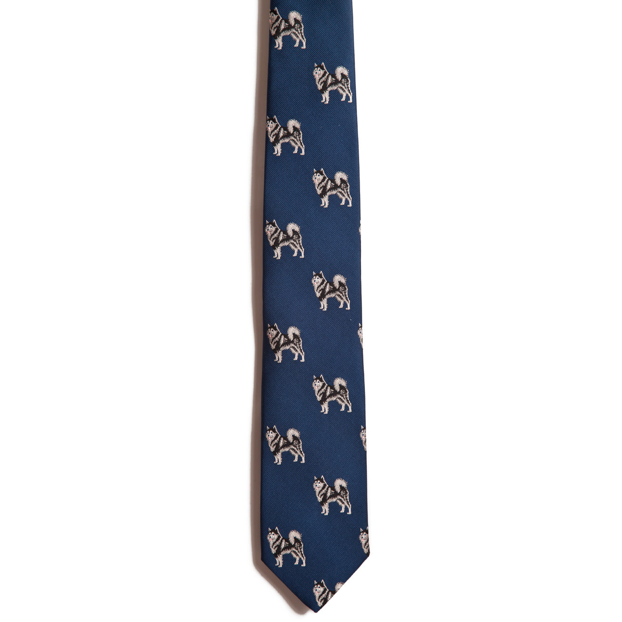 The Alden Madison Alaskan Malamute tie is a blue silk jacquard necktie featuring a repeating pattern of small, embroidered Alaskan Malamutes in white, gray, and black, standing out on the solid background.