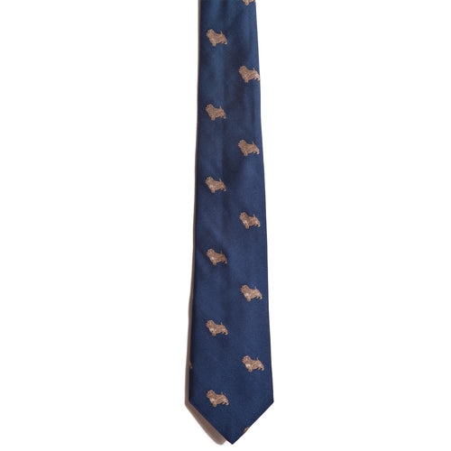 The Alden Madison Norfolk Terrier silk dog tie showcases a blue background with a repeating pattern of small, embroidered beige Norfolk Terriers, displayed against a white backdrop.