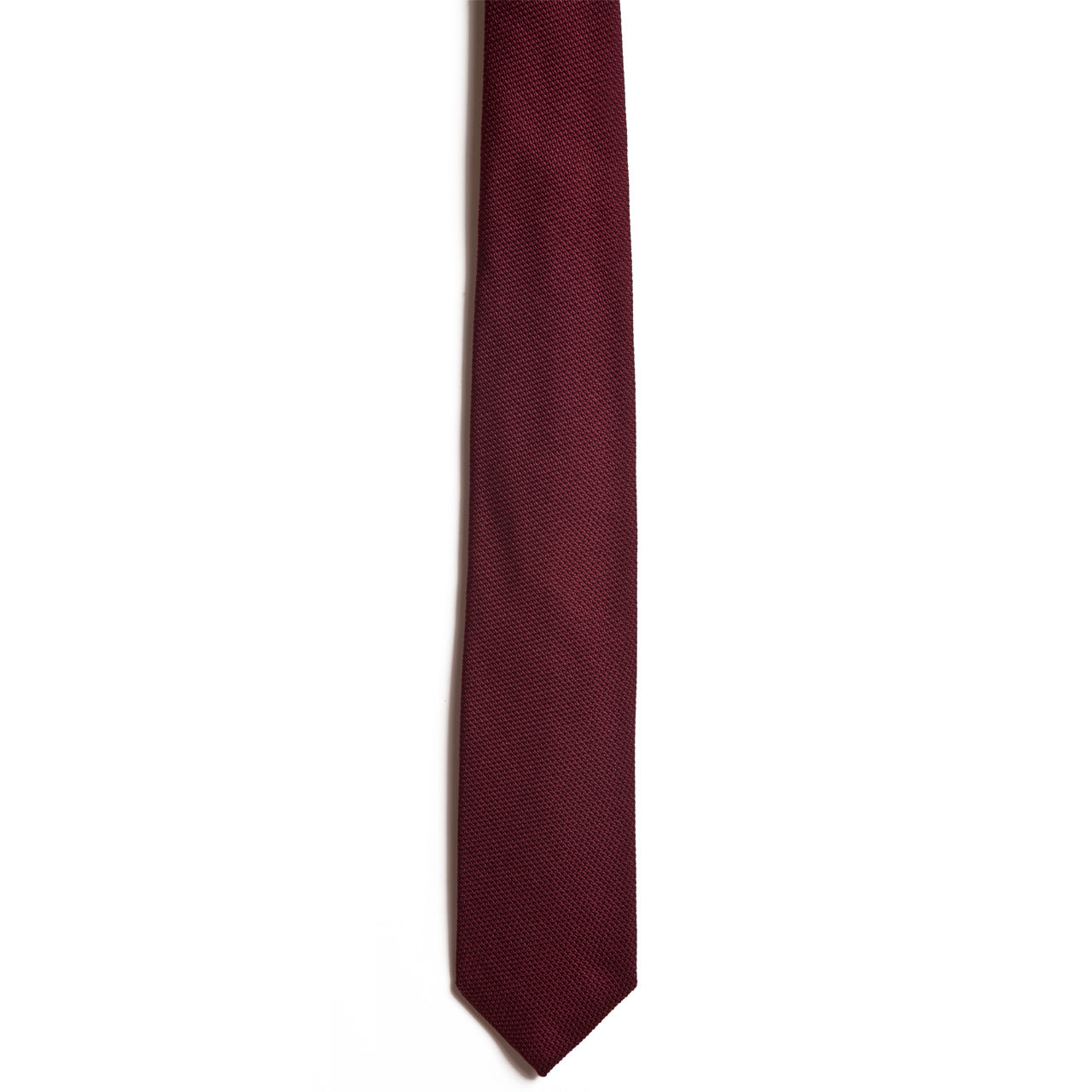 A close-up image of a maroon necktie, the Wine by Alden Madison, crafted from Italian silk against a white background. The tie is vertically oriented with textured fabric and features a classic pointed tip.