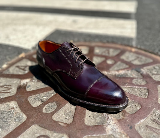 The Alden Madison 2160 - Cap Toe Blucher in Color 8 Shell Cordovan, featuring a Double Oak Leather Outsole, is displayed on a decorative metal manhole cover with a blurred street and crosswalk in the background.