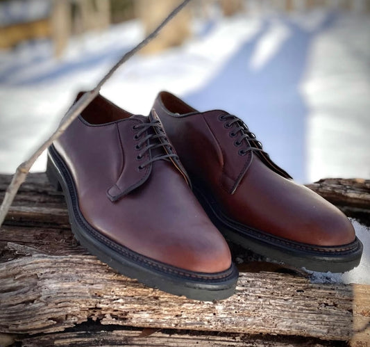 The Alden Madison 9432S Plain Toe Blucher in Brown Chromexcel, featuring Lug Rubber Soles and a Barrie last, is displayed outdoors on a weathered wooden surface with snow in the background.