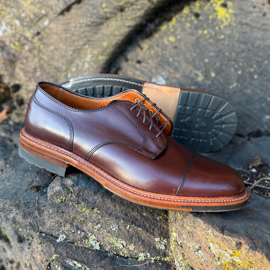 The ALDEN SHOES 22531C - Brown Calf DeRosa Cap Toe bluchers with tan commando soles are shown outdoors on a rock, one upright and the other on its side to highlight the rugged tread.