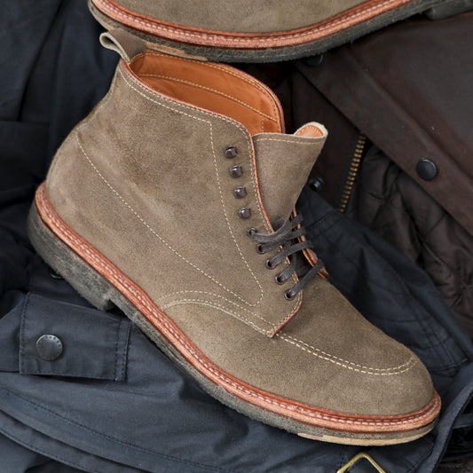 An ALDEN SHOES D6966H - Clay Suede Indy Boot, featuring visible stitching and a brown sole, crafted on the Trubalance Last, rests atop dark quilted fabric accented with buttons and a zipper.