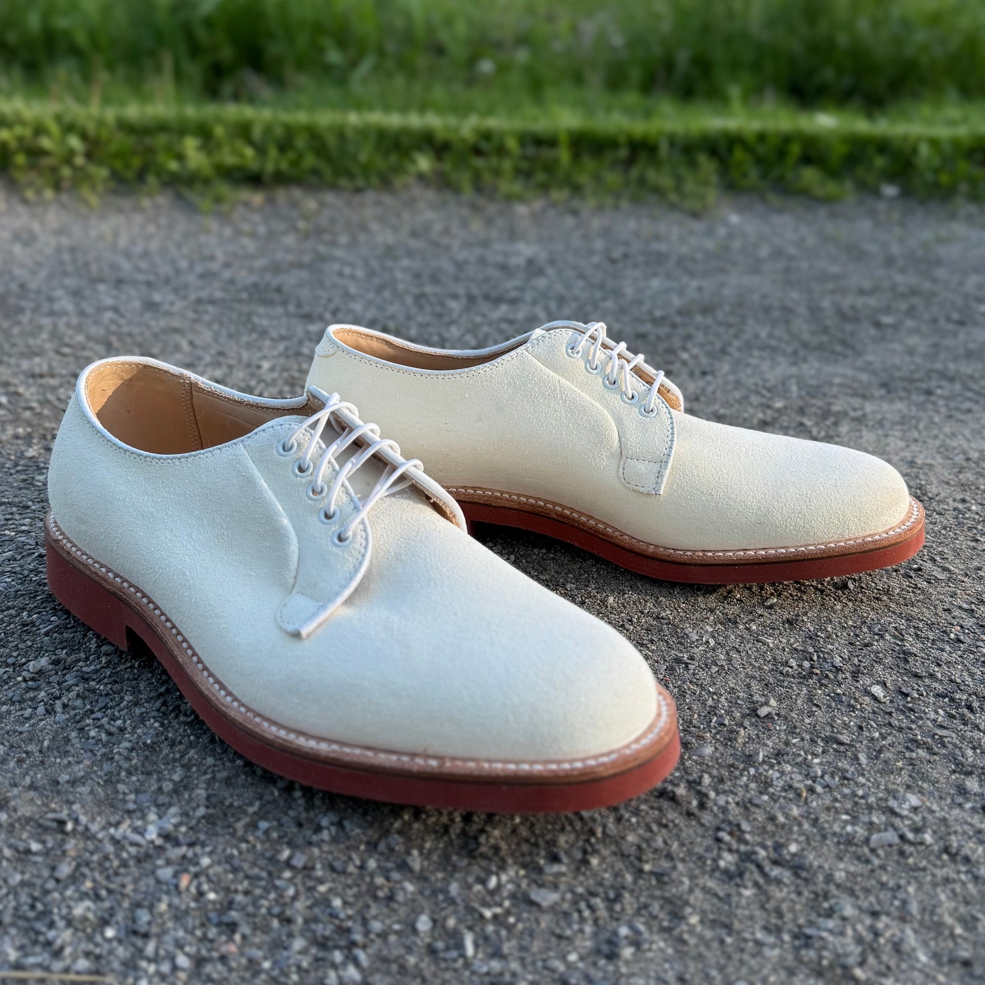 Alden Madisons 9448 - White Buck in Ivory Suede oxford shoes with Red Microcell Soles and white laces, shown on gravel with green grass behind.