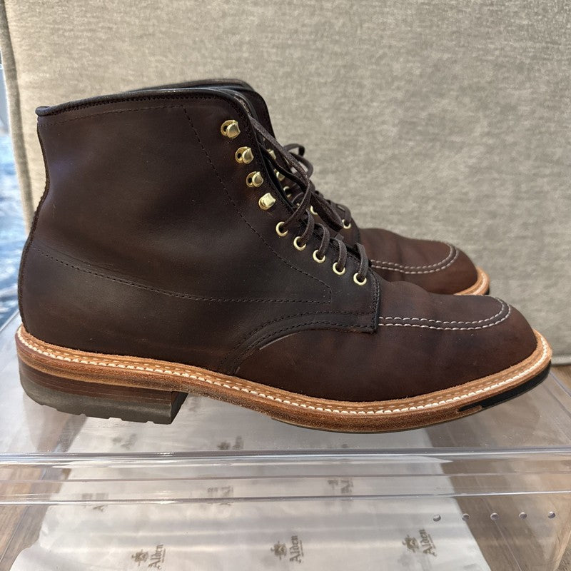 A pair of ALDEN SHOES D5920HC Kudu Indy boots in dark brown Chromexcel leather with light brown stitching, tan welt, metal eyelets, and Commando sole, crafted on the Trubalance last and displayed on a clear acrylic stand with gray fabric background.