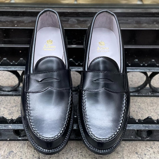 Alden Madison 987 - Leisure Hand Sewn Black Shell Cordovan penny loafers with stitching details are displayed side by side on stone, showcasing the gold Alden logo insole and a durable Single Oak Leather Outsole.