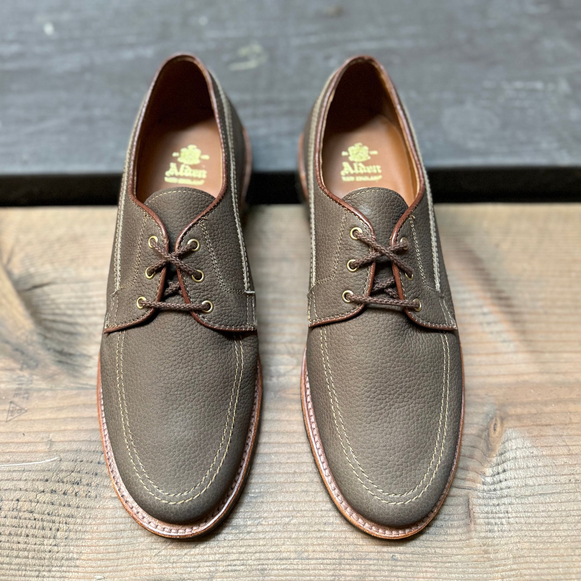 Alden Madison’s 7351 - Ivy Blucher in Clay Nubuck leather with tan stitching are lace-up dress shoes shown side by side on a wooden surface.