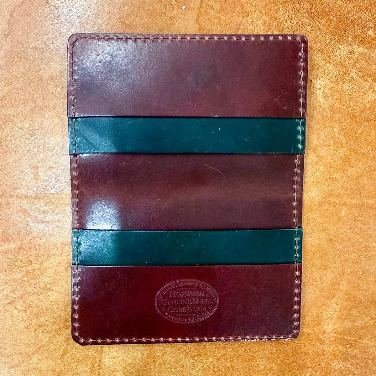 Alden Madison Credit Card Wallet in Shell Cordovan, a dark burgundy shell cordovan card wallet featuring two dark green horizontal pockets and an embossed logo stamp at the bottom.