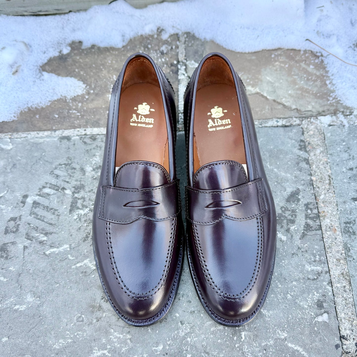 A pair of ALDEN SHOES 96948 - Copley Penny Loafer in Color 8 Shell is placed side by side on a stone surface, with snow visible in the background.