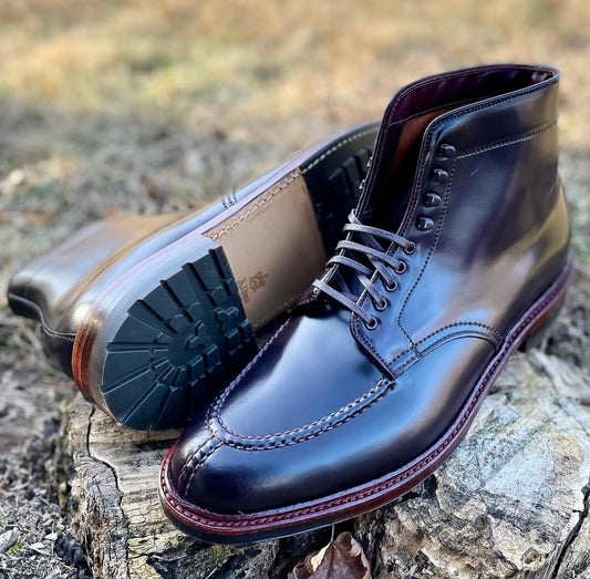 A pair of Alden Madison 40218HC - NST Tanker Boots in Color 8 Shell Cordovan with visible stitching, one upright and one on its side, displayed outdoors on a tree stump. They feature the classic Barrie Last for comfort.
