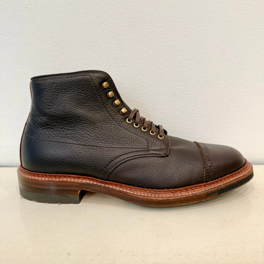 The Alden Madison D9819HC - Jumper Boot in Regina Brown Grain is a single brown calfskin leather boot featuring a textured surface, cap toe, brass eyelets, brown laces, sturdy midsole, and black Commando sole. The elegant boot is displayed against an off-white background.