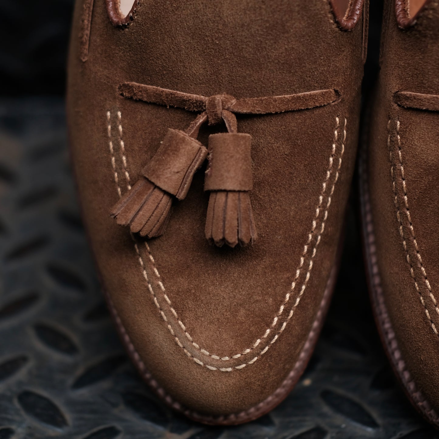 Close-up of Alden Madisons 3403 Tassel Loafer in snuff suede, featuring tassels and white stitching, crafted on the Aberdeen Last and displayed on a dark textured surface.