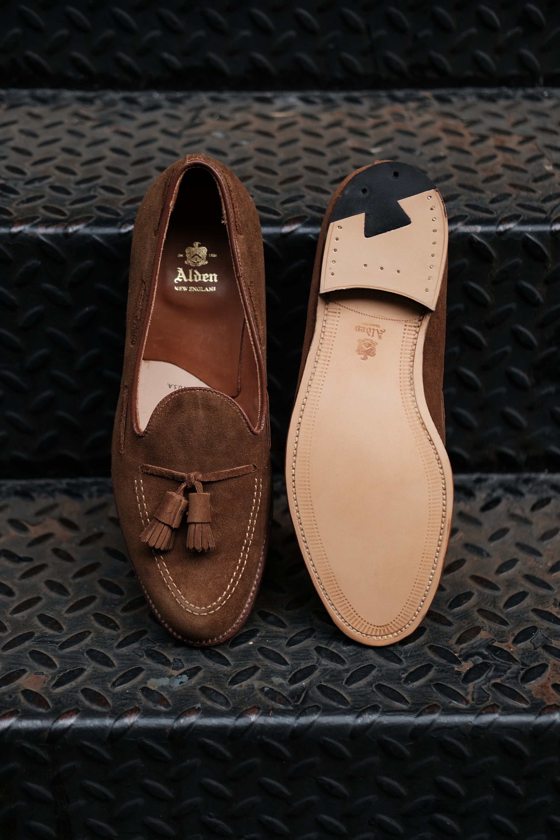 Alden Madison’s 3403 - Tassel Loafer in Snuff Suede is shown on a black metal stair, with one shoe displaying the top and the other showcasing the leather sole.