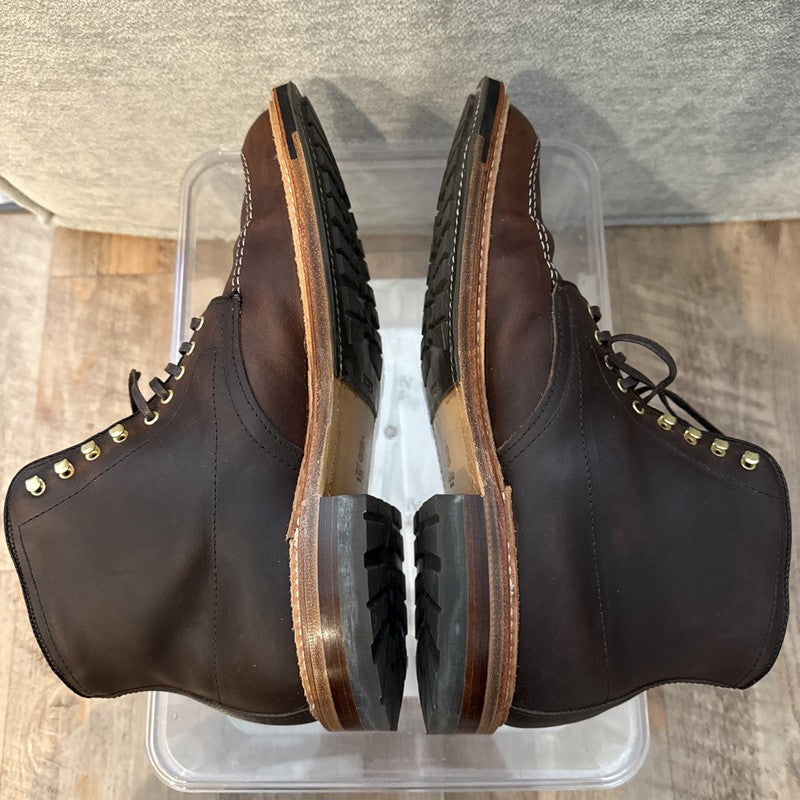 A pair of ALDEN SHOES D5920HC - Kudu Indy w Commando Sole boots in brown leather with gold eyelets, black rubber soles, and Trubalance Last, shown side by side on a clear plastic box, highlighting the sturdy tread from above.