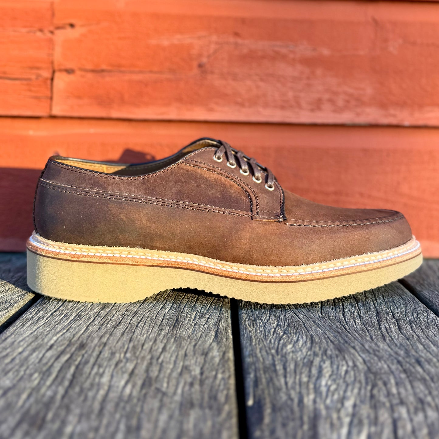An ALDEN SHOES 73980 Tobacco Chamois Ranger Mocc with Wedge rests on a wooden surface.