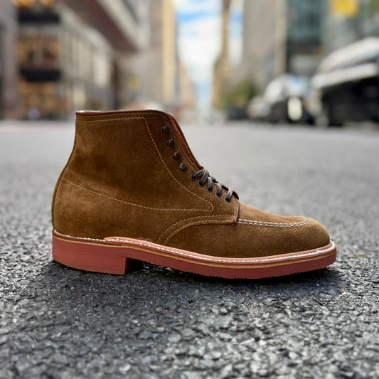 The Alden Madison 40531H - Redwood Indy Boot in Snuff Suede, featuring a red rubber sole and Trubalance Last, stands on an empty city street with blurred buildings and cars in the background.