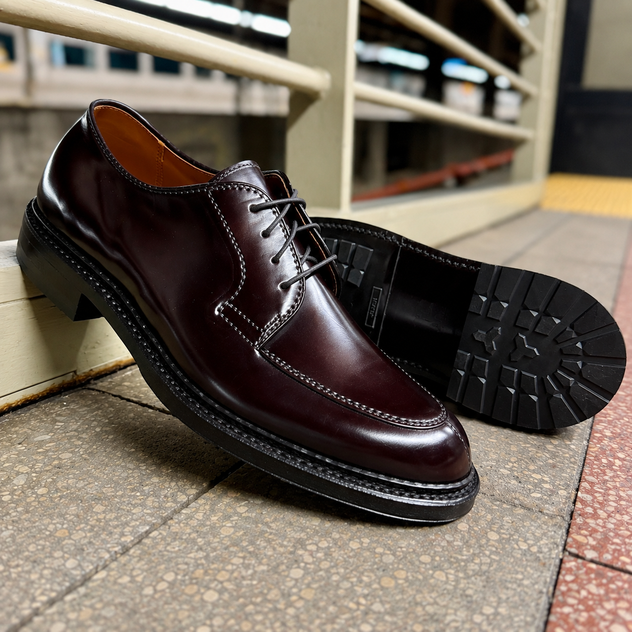 A pair of ALDEN SHOES D6632C - Borough Blucher in Color 8 Shell, crafted from polished dark brown Shell Cordovan leather, are displayed with one shoe upright and the other on its side revealing the sole, positioned on a tiled surface near a metal railing.