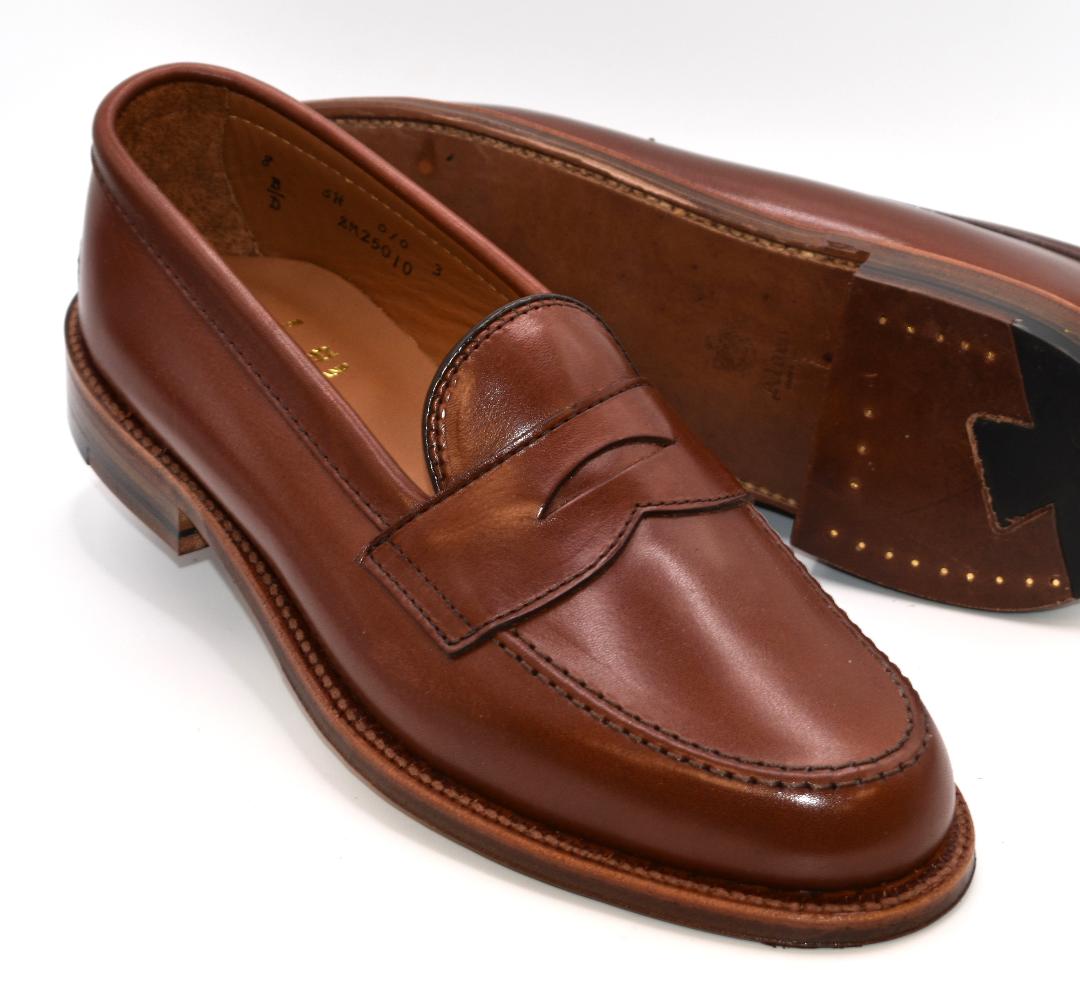 Alden Madison’s 9826 Penny Loafer in Walnut Michigan Calf features stitched detailing, a flex oiled leather sole, and is crafted on the Van Last—shown with one shoe upright and the other displaying its sole and heel.
