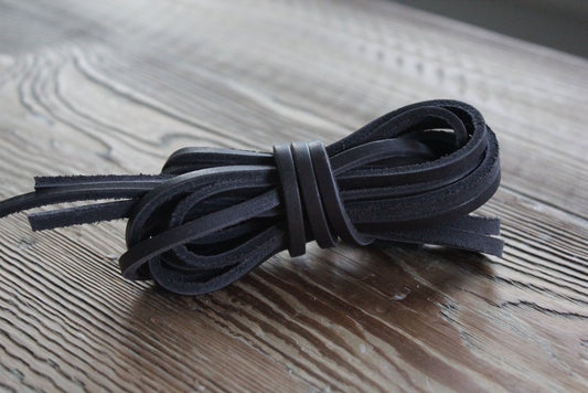 A set of Alden Madisons Rawhide Laces in Black, custom cut to a length of 74 inches, elegantly adorns a textured wooden surface. Ideal for Guarded Goods.