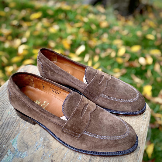 The Alden Madison 9697F - Flex Penny Loafer in Brown Suede is showcased outdoors on wood, featuring a sleek Copley Last design with visible stitching and a Flex Leather Sole, against green grass and scattered yellow leaves.