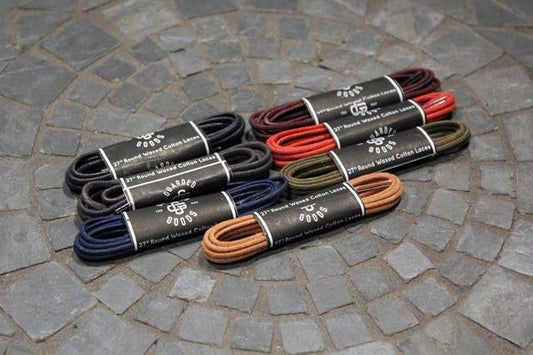 Nine pairs of Alden Madison Shoe Lace Guarded Goods, 27-inch waxed cotton laces in assorted colors, each wrapped with a black band, are displayed on a mosaic stone surface.